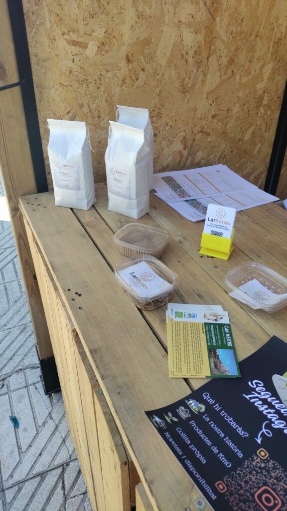 Taula de l'estand amb paquets de FrassBo, mostres i flyers d'altres expositors de proximitat